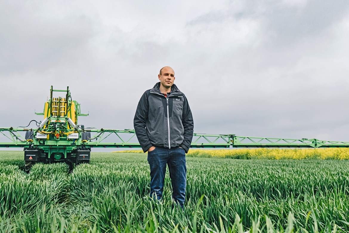 Mann auf Weizenfeld, Agrarmaschine im Hintergrund