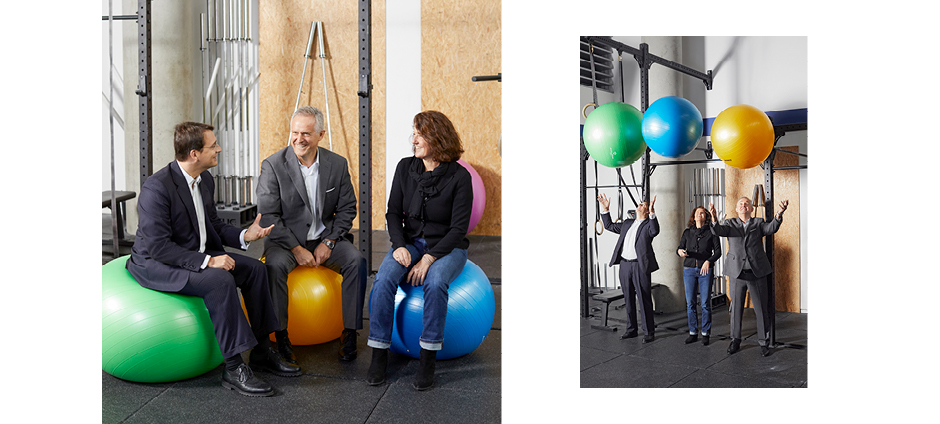 Jochen Haug, Stefan Lauer und Birgit Bals sitzen auf Gymnastikbällen und werfen diese in die Luft