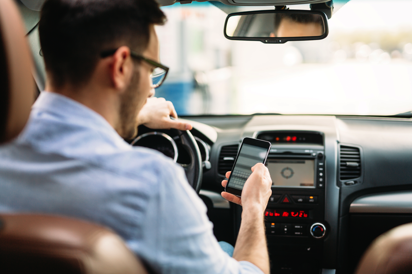 Ein Mann fährt ein Auto, während er auf sein Handy blickt.