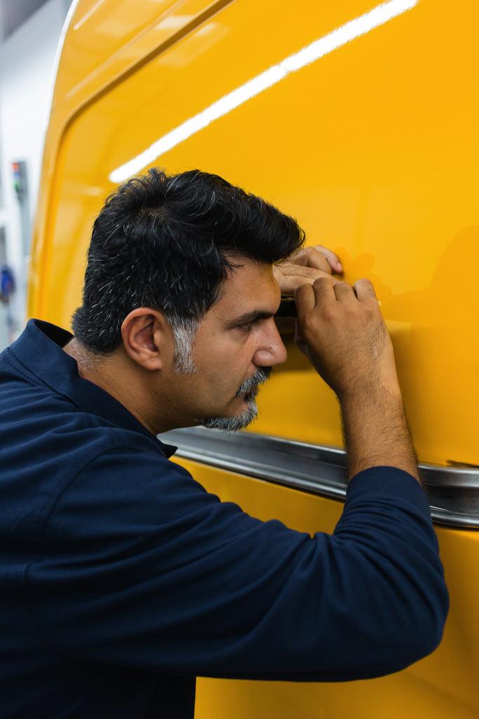 Der Farbexperte Kuddusi Yilmaz inspiziert die gelbe Karosserie eines Wagens mithilfe einer Lupe.