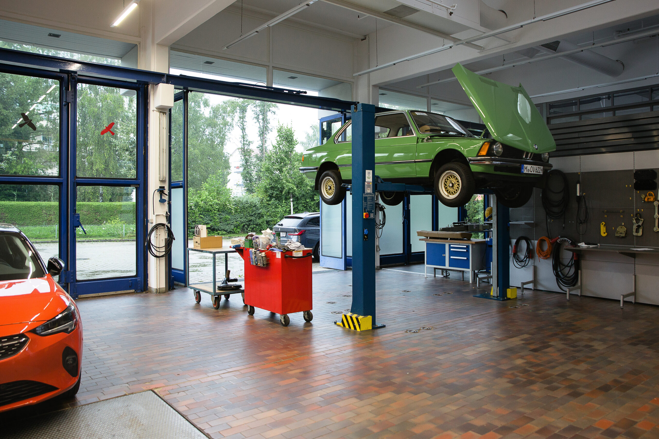 Ein orangenes Auto und ein grüner Oldtimer werden in der Werkstatt des Allianz Zentrum für Technik unter Augenschein genommen.