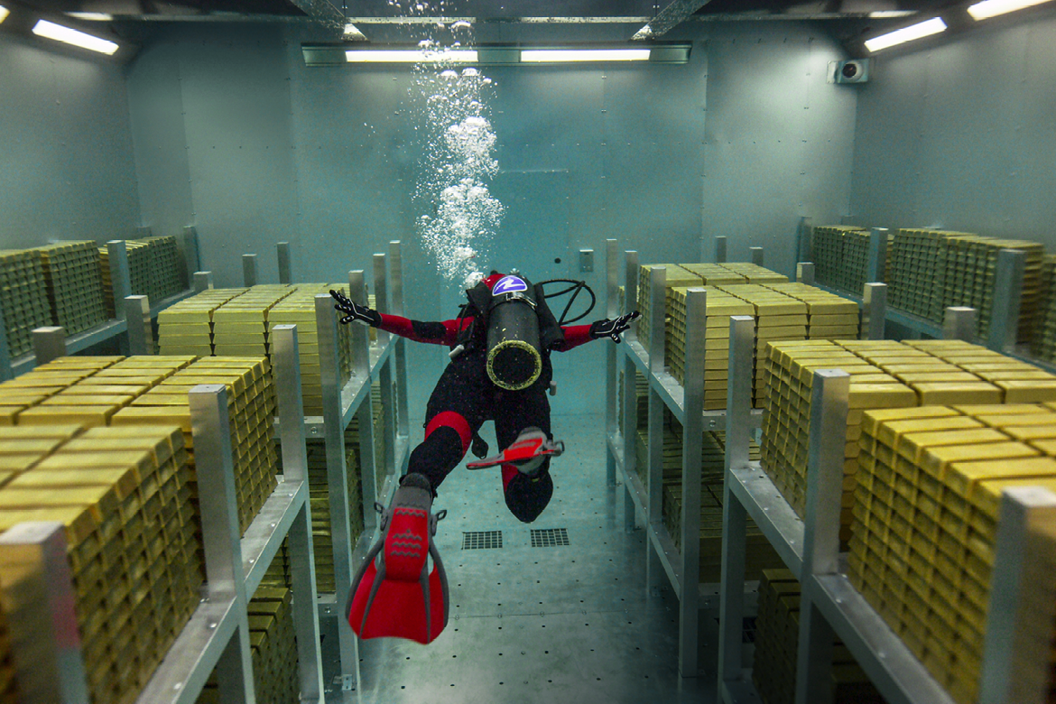 Ein Unterwassertaucher schwimmt zwischen Paletten voll Goldbarren entlang.