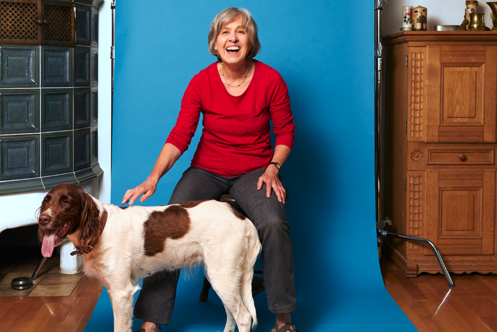 Angelika Kiefmann sitzt mit ihrem Hund Inka vor einer blauen Leinwand.