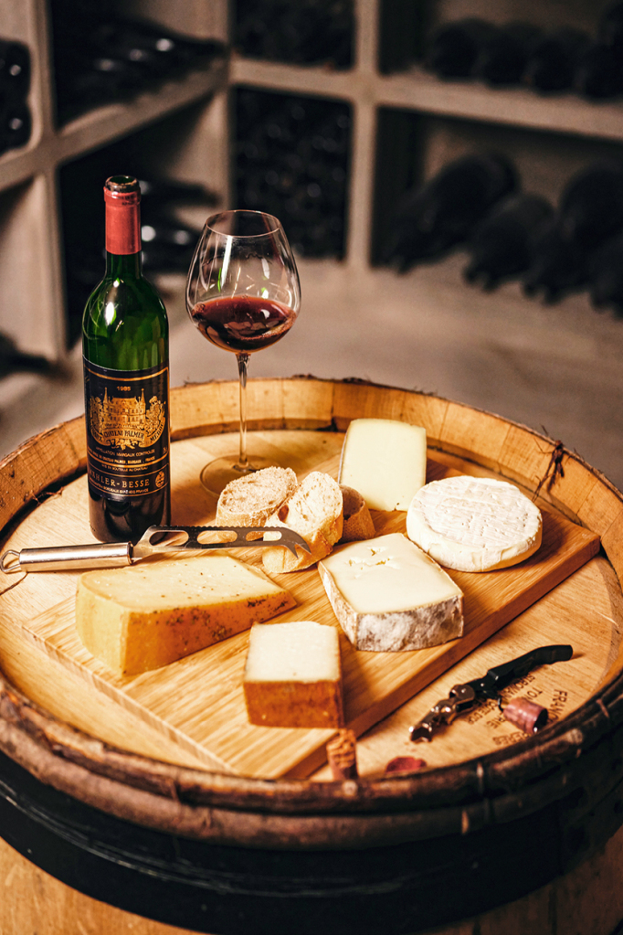 Auf einem Serviertablett wurde eine Flasche Rotwein inklusive Glas mit verschiedenen Käsesorten angerichtet.