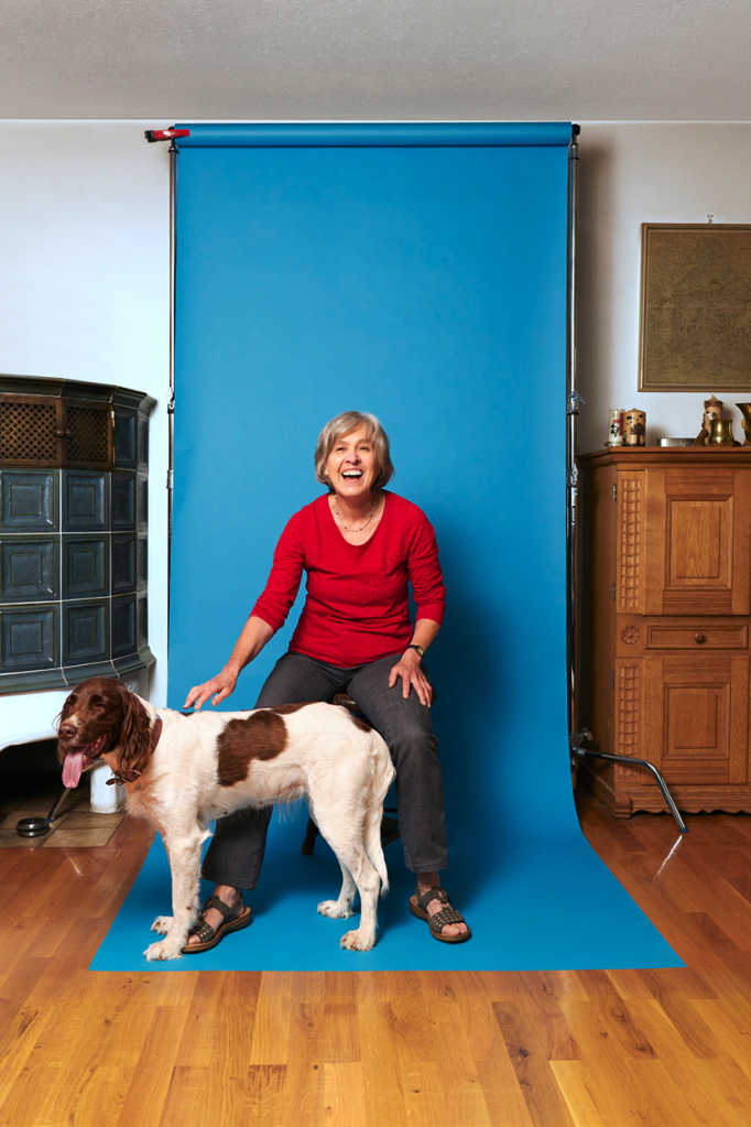 Angelika Kiefmann sitzt mit ihrem Hund Inka vor einer blauen Leinwand.