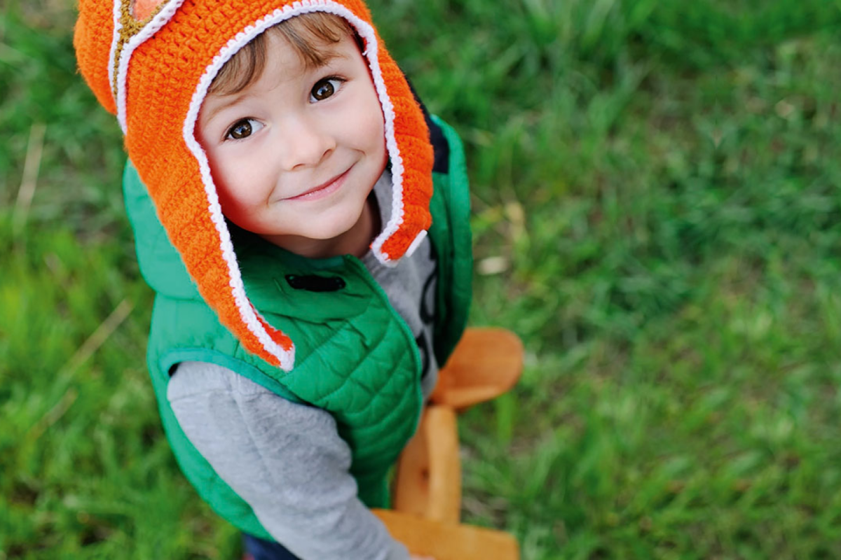 Ein kleiner Junge mit orangener Mütze steht auf einer grünen Wiese.
