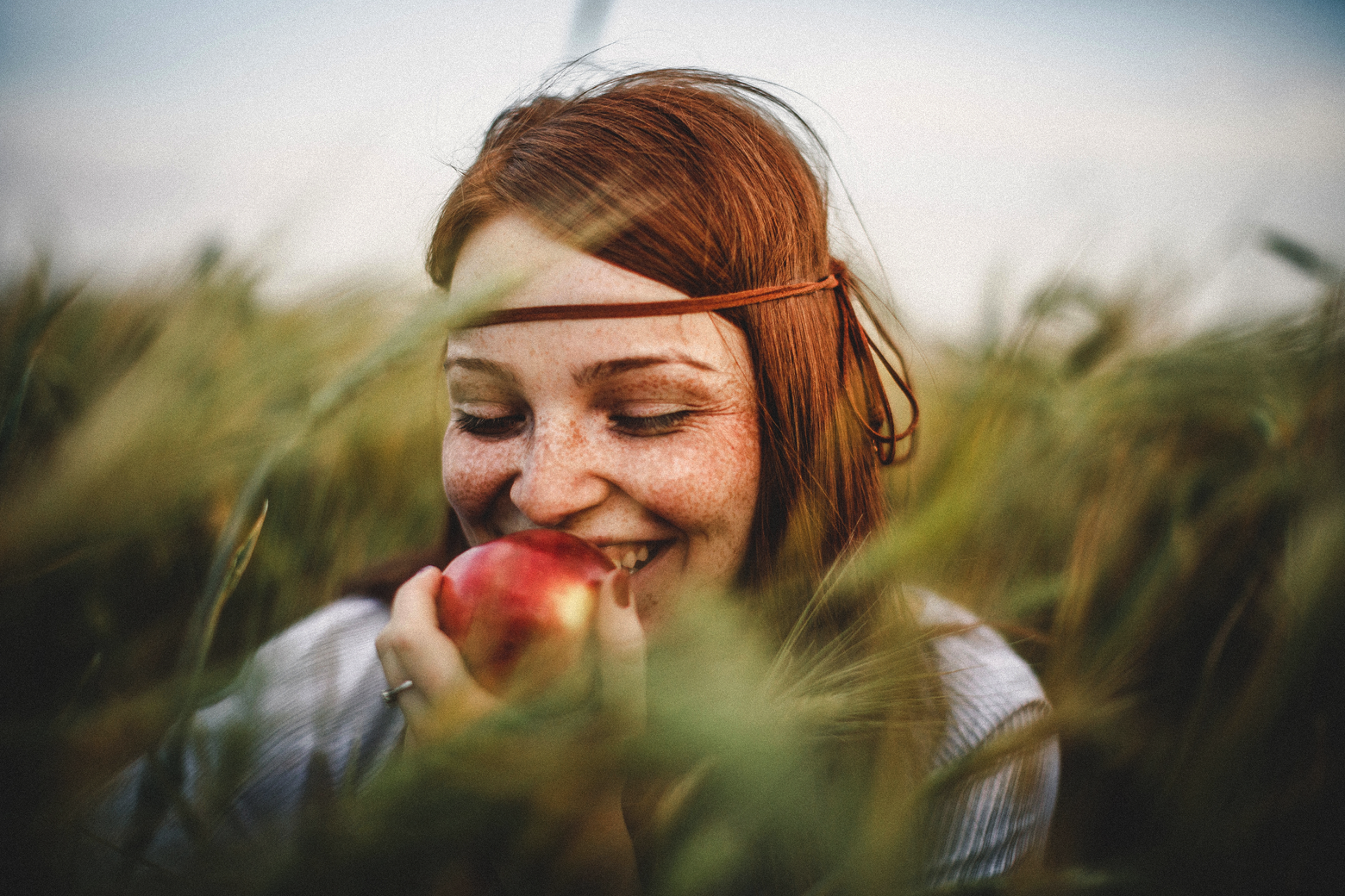 Junge Frau sitzt in einem Feld und beißt in einen Apfel