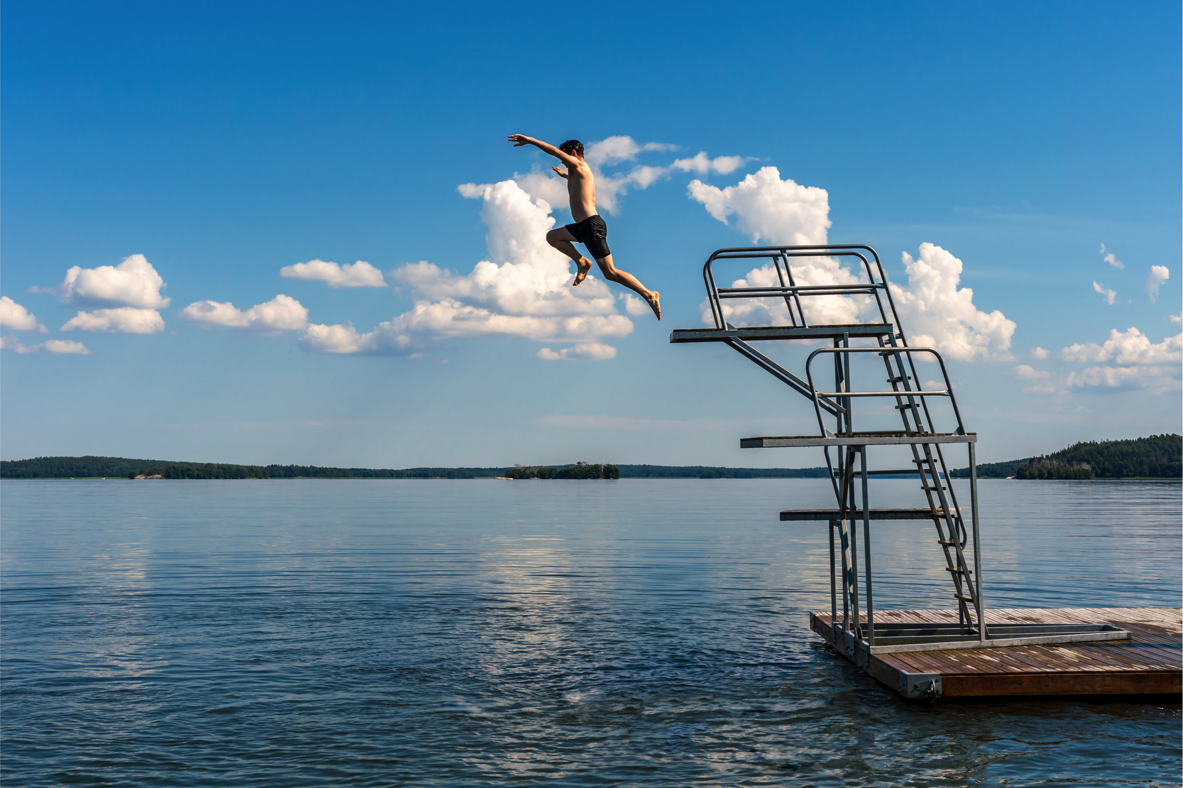 Ein Junge springt von einem Sprungturm in einen See