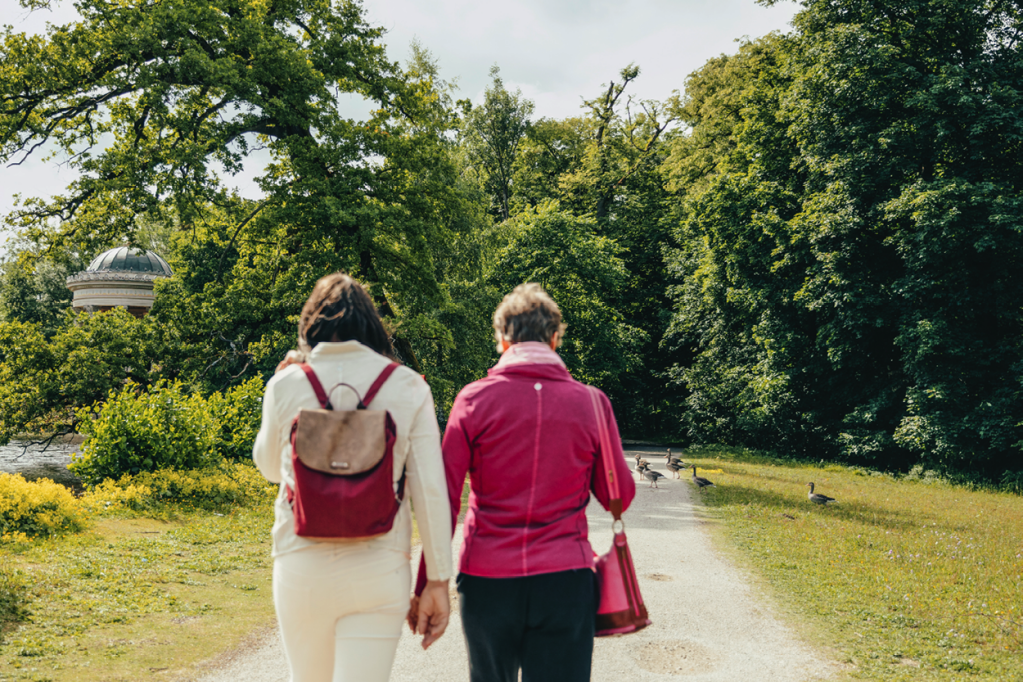 Von hinten fotografiert: Charlotte und Karoline laufen Hand in Hand einen Weg im Park entlang