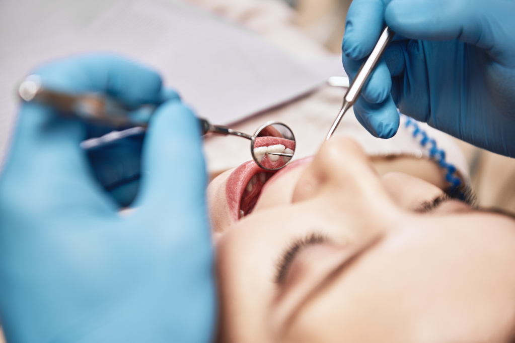 Nahaufnahme einer Frau, die ihren Mund weit geöffnet hat. Der Zahnarzt untersucht ihre Zähne mit zahnärztlichen Werkzeugen.