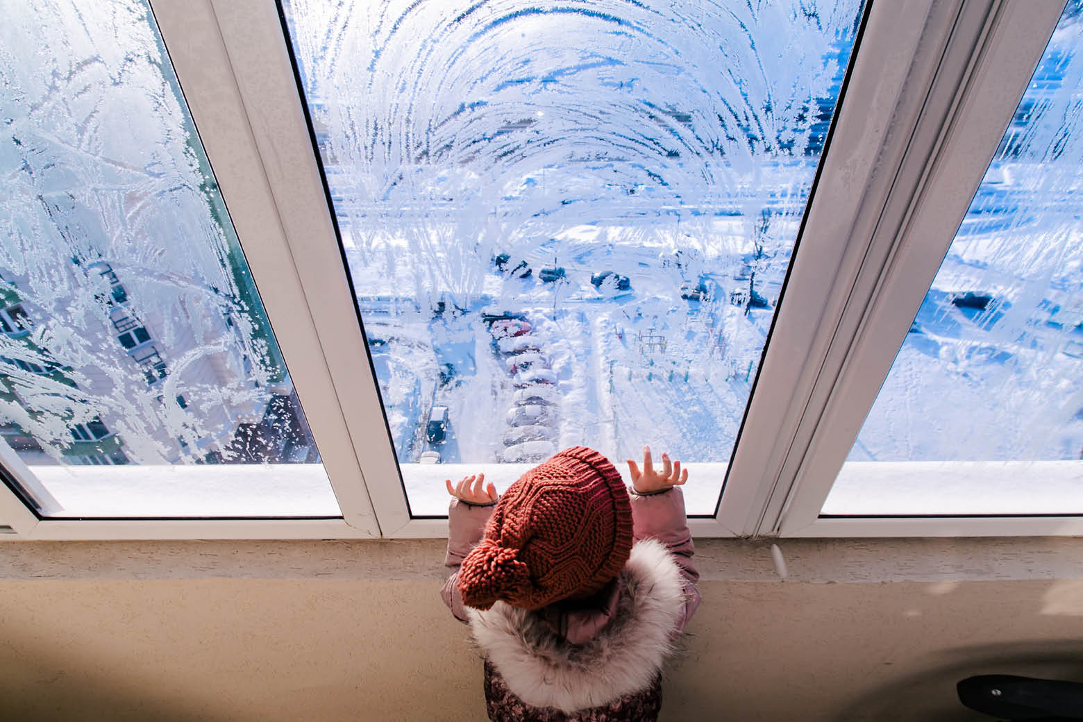 Kind schaut aus dem Fenster auf eine verschneite Straße und Landschaft